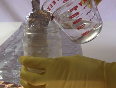 The homemade electrolytic capacitor in a container with more 
      electrolyte being poured in.